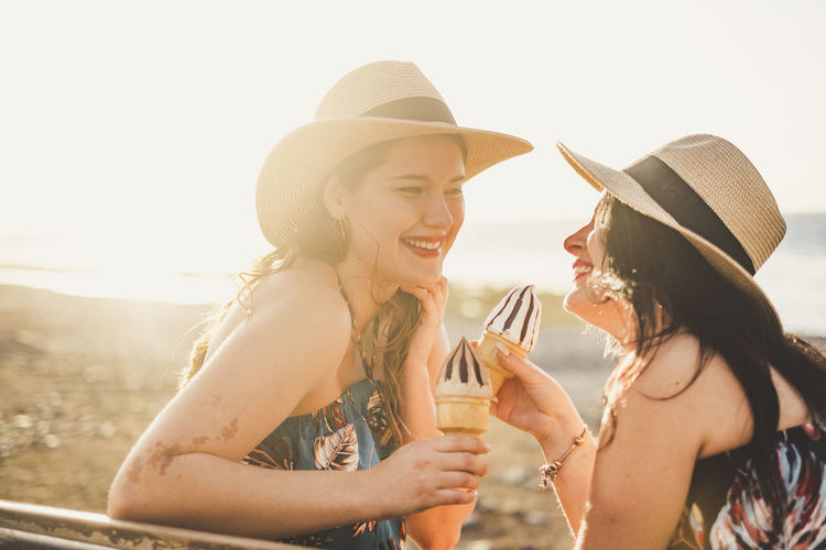 Side view of lesbian woman holding ice creams against sky