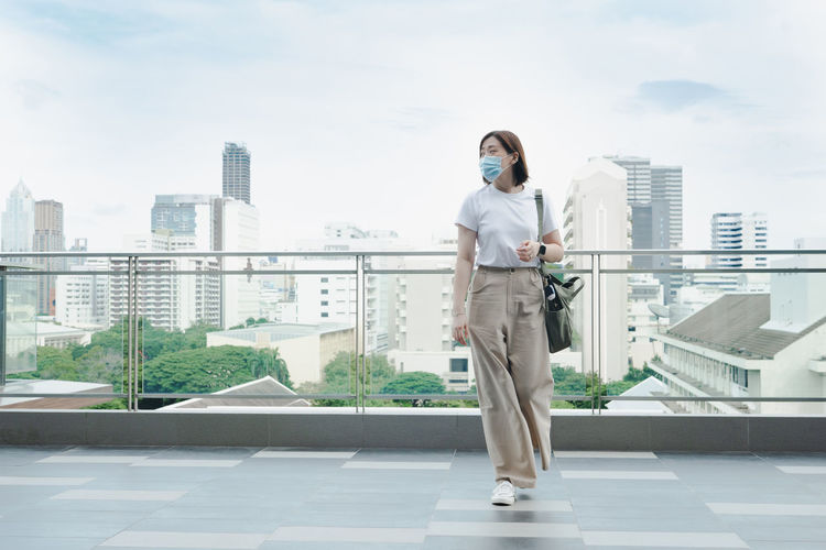 Solo asian woman wear protective mask during outdoor break and relax at rooftop with city background