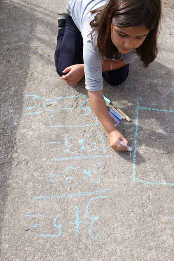 High angle of girl writing with chalk on footpath