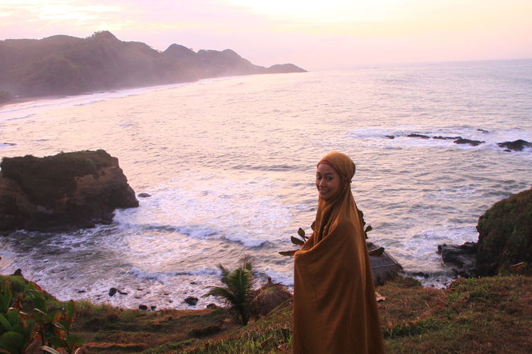 Portrait of woman in headscarf while standing on beach during sunset
