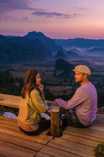 Side view of woman sitting on mountain against sky during sunset