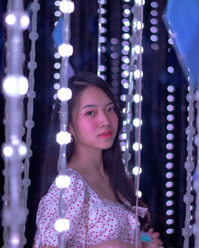 Portrait of young woman standing amidst illuminated lights