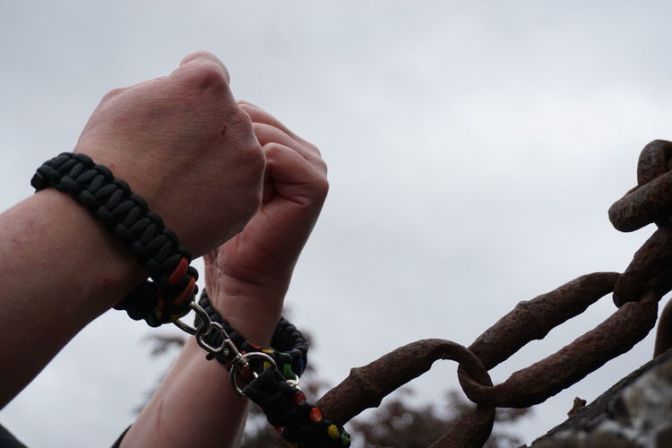 Cropped hands attached with metallic chain against sky
