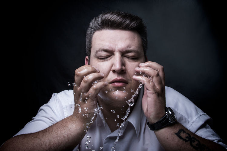 Portrait of young man making face against black background