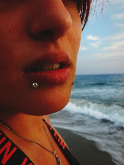 Midsection of young woman standing at beach against sky during sunset
