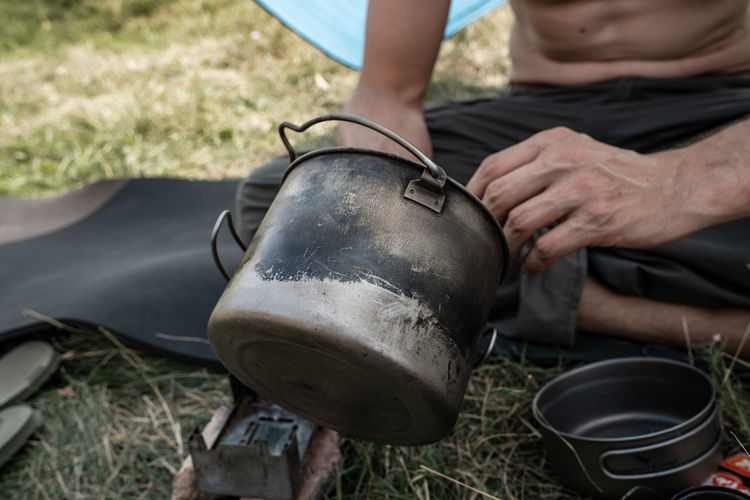 Midsection of man holding titanium vooking pot outdoors