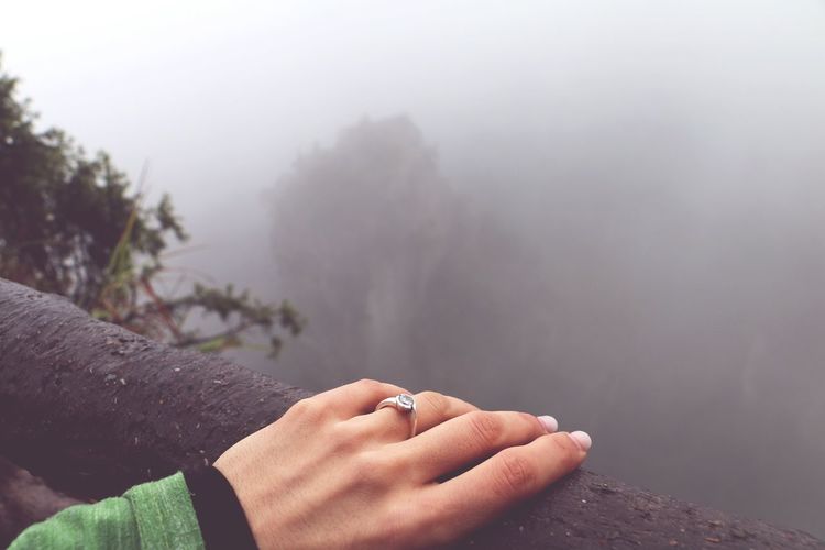 Cropped hand of woman on railing during foggy weather
