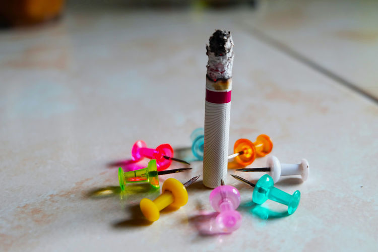 Close-up of cigarette amidst multi colored thumbtack on table