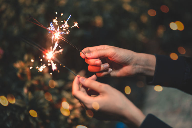 Cropped hands of woman holding lit sparklers at night