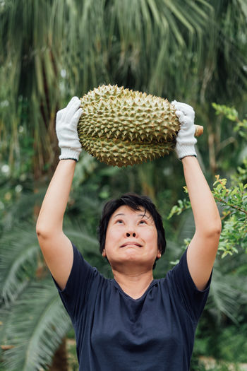 Close-up of woman holding durian against trees