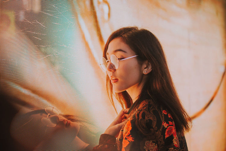 Close-up of young woman standing against illuminated city at night