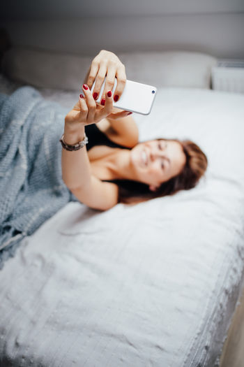 Woman taking selfie through mobile phone while lying on bed