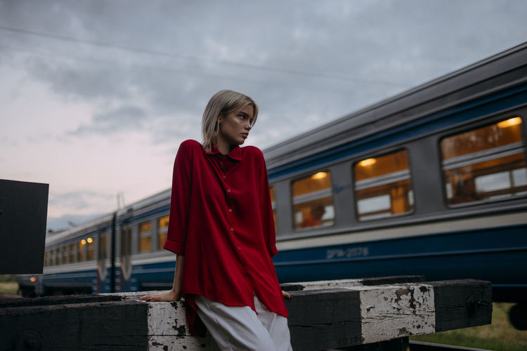 A blonde woman in a red shirt stands near a passing train