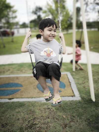 Full length of smiling boy enjoying on swing at park