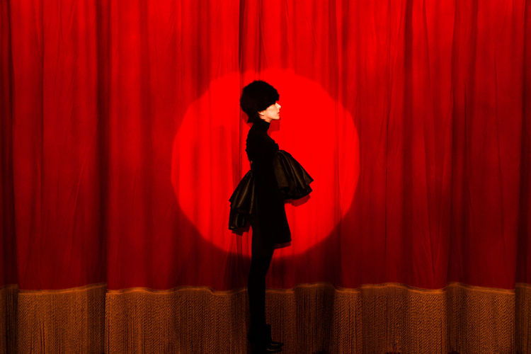 Full length of woman standing against red curtain