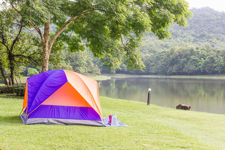Tent on grass by lake against trees