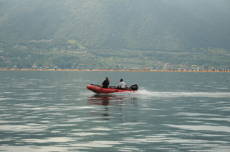 People in boat on sea against mountain