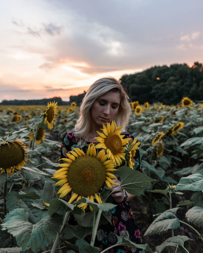 Woman amidst sunflowers on field against sky during sunset