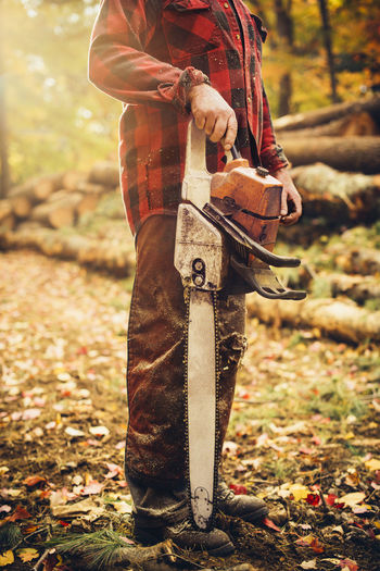 Low section of lumberjack holding chainsaw in forest