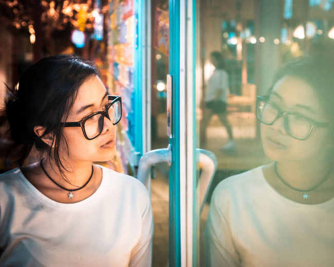 Woman wearing eyeglasses looking in window at night