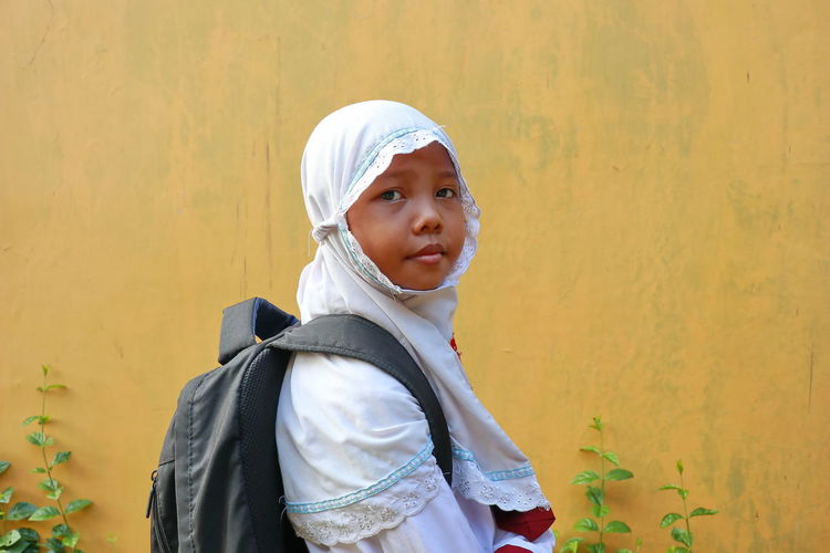 Portrait of schoolgirl standing against wall