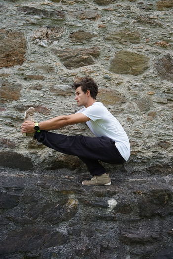 Young man exercising by stone wall