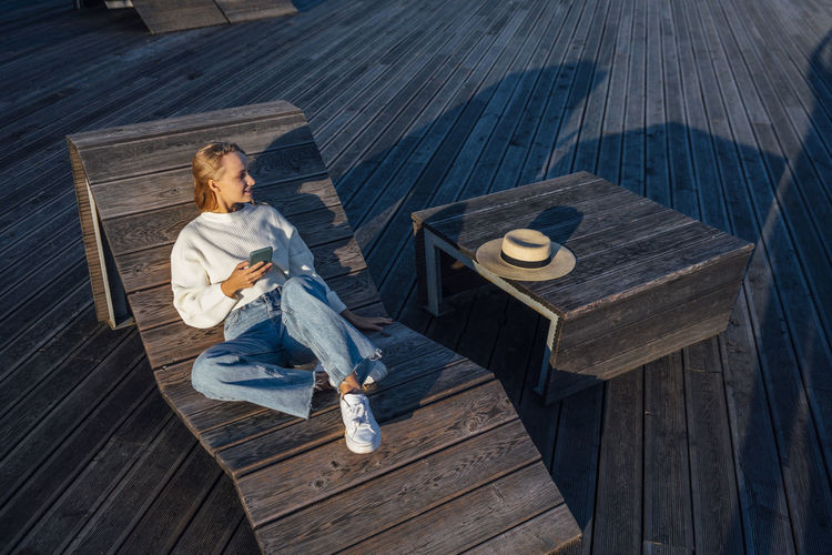 Woman with smart phone sitting on wooden bench