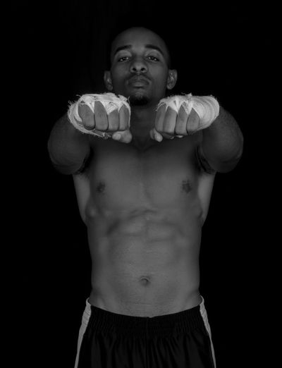 Portrait of shirtless muscular man with wrapped hands against black background
