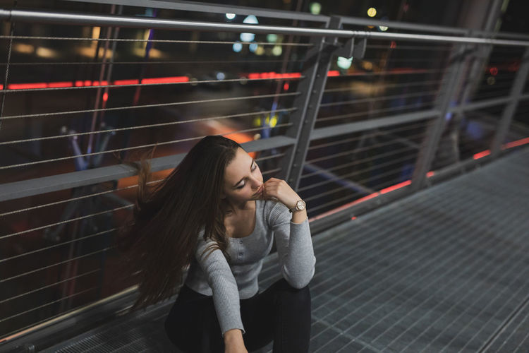 High angle view of woman looking away while sitting on footbridge at night