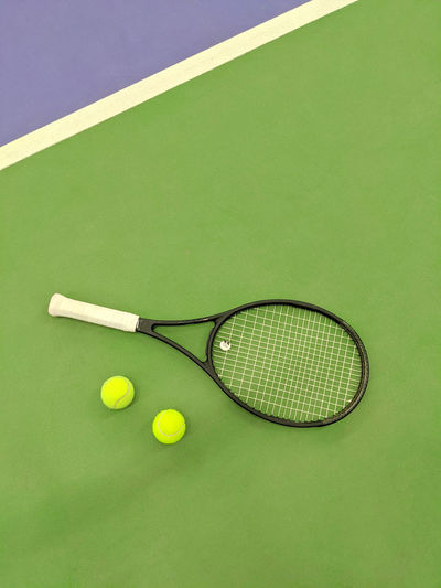 Top view of tennis racket and two balls on the green clay tennis court.