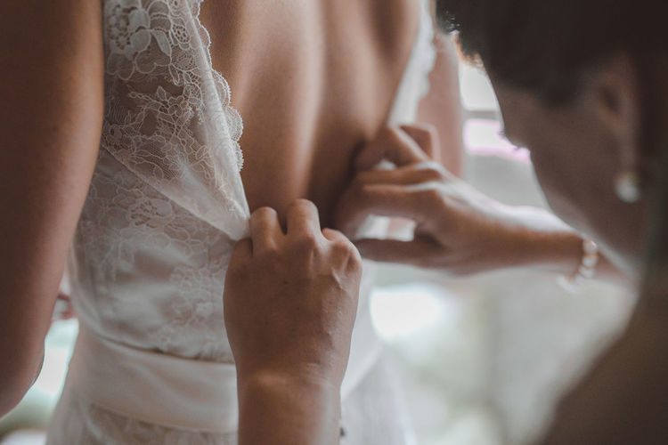 Bridesmaid helping bride with dressing in bedroom during wedding