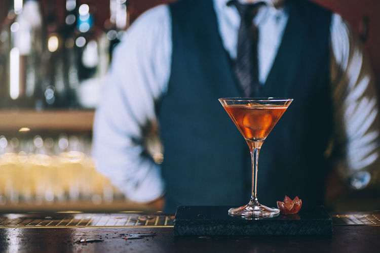 Midsection of mature bartender standing by cocktail on bar counter