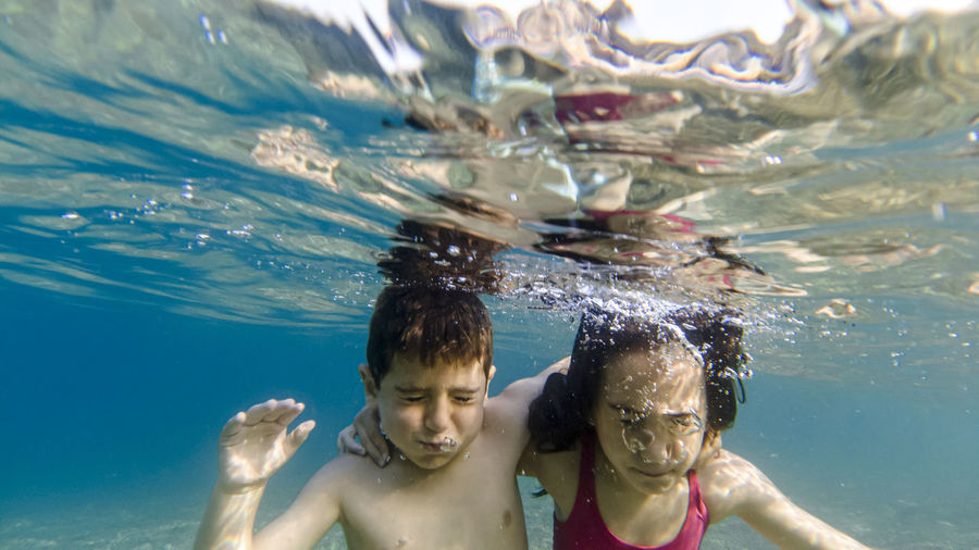 Siblings swimming underwater in pool