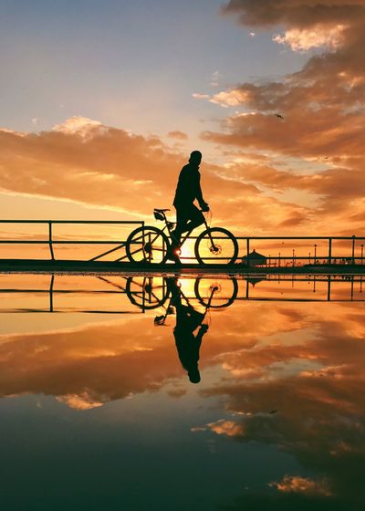 Silhouette man bicycle on bridge against sky during sunset
