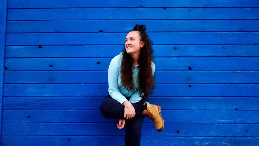 Smiling young woman standing against blue wooden wall