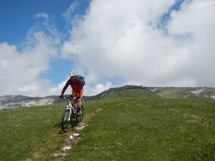 Cyclist riding bicycle on grassy field against cloudy sky