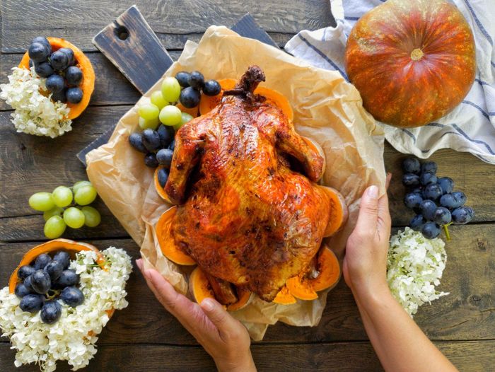 In the hands of a girl, a freshly cooked thanksgiving turkey decorated with pumpkins, grapes
