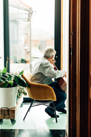Elderly man playing on acoustic guitar at home. senior person with music hobby.