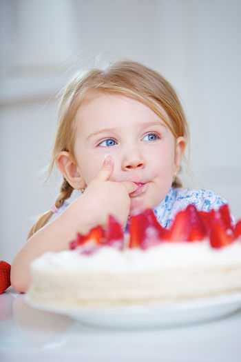 Cute girl looking away while eating strawberry cake at home