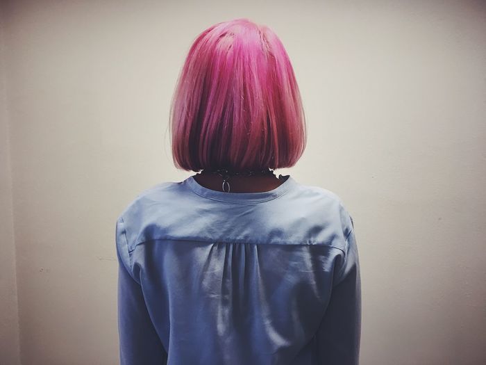Rear view of woman with pink hair standing against wall at home