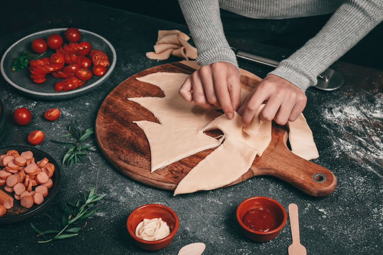 Hands of a girl separate the christmas tree from a thin one on pizza dough on a cutting board 