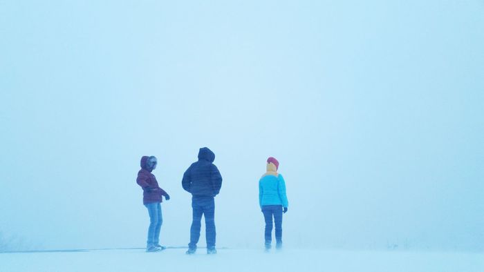 Friends standing on snowy landscape against clear sky during winter