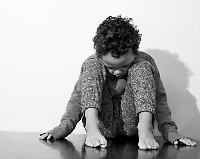Full length of sad boy sitting on floor against wall