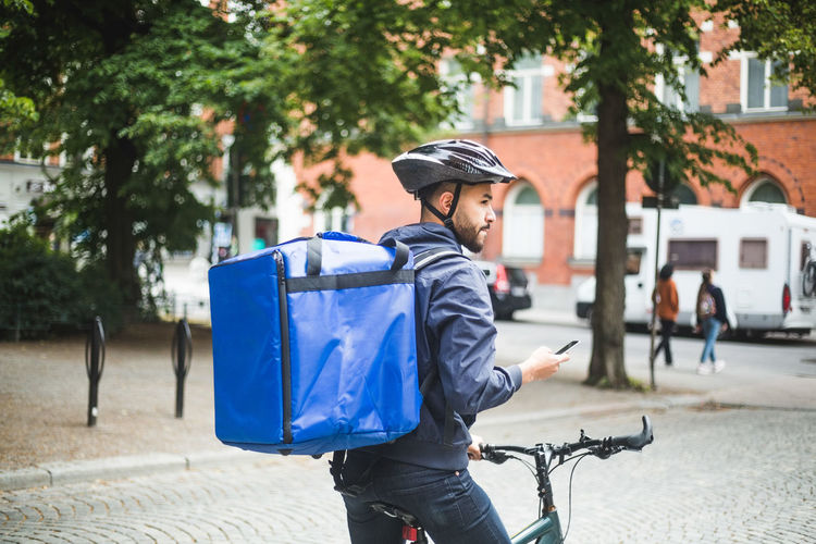Food delivery man with bicycle looking away while standing on street in city