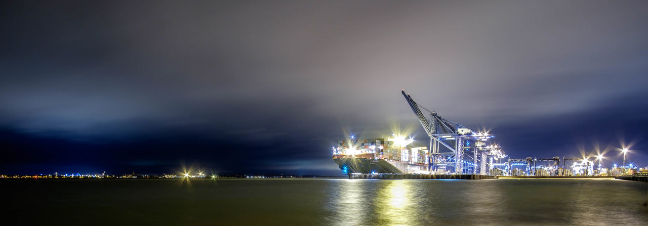 Panoramic shot of sea by illuminated dock against sky at night