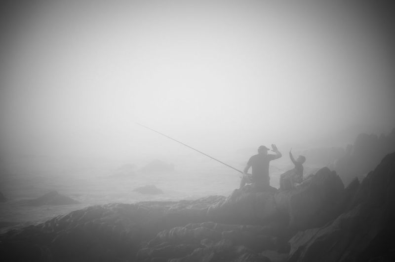 Man fishing on mountain against sky