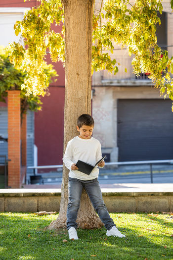 Little kid reading a book in a shade of a tree