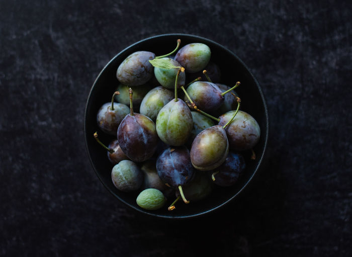 Overhead shot of a bowl of fresh plums against a black background.