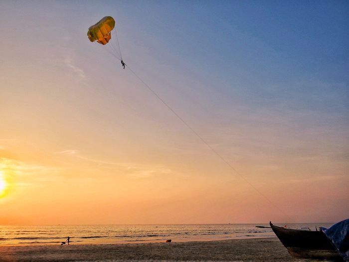 People paragliding on beach against sky during sunset
