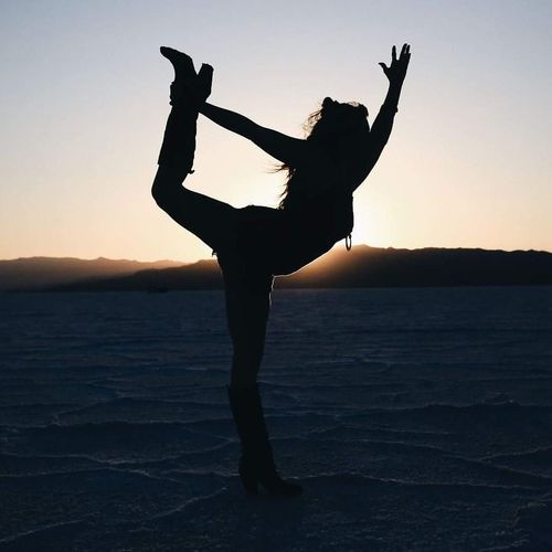 Silhouette woman stretching on salt flats against sky during sunset